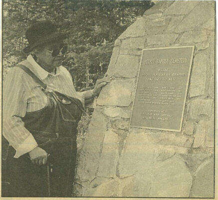 Oretha Allen standing next to a cairn at the Bethel Baptist Cemetery in the Campsie community