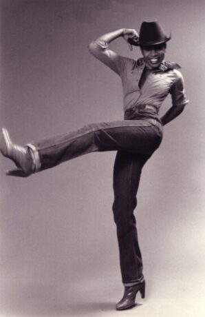 Black and white photo of Lovenna Fox smiling and kicking her left leg up.