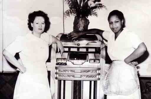 Two unidentified women standing in front of a jukebox